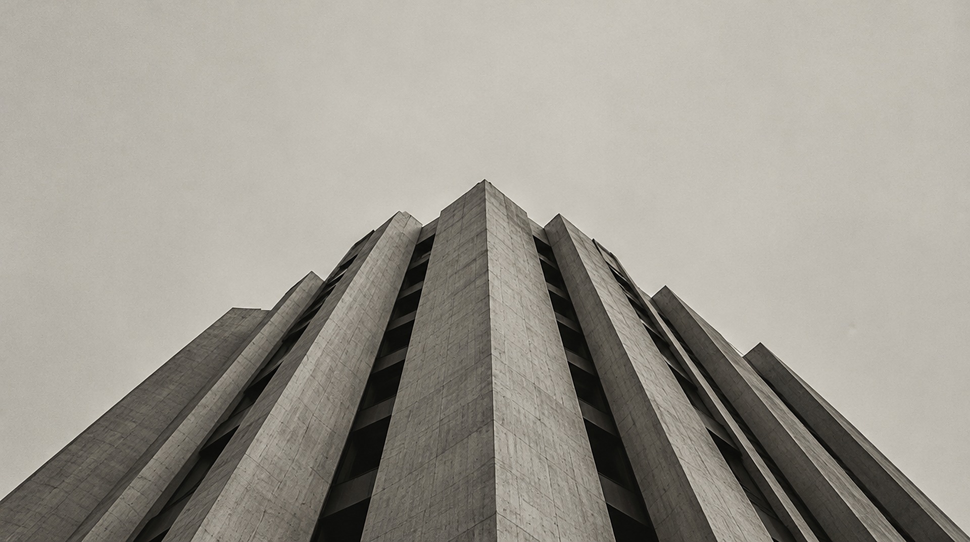 Fachada de concreto brutalista fotografada de baixo, contra um céu claro.