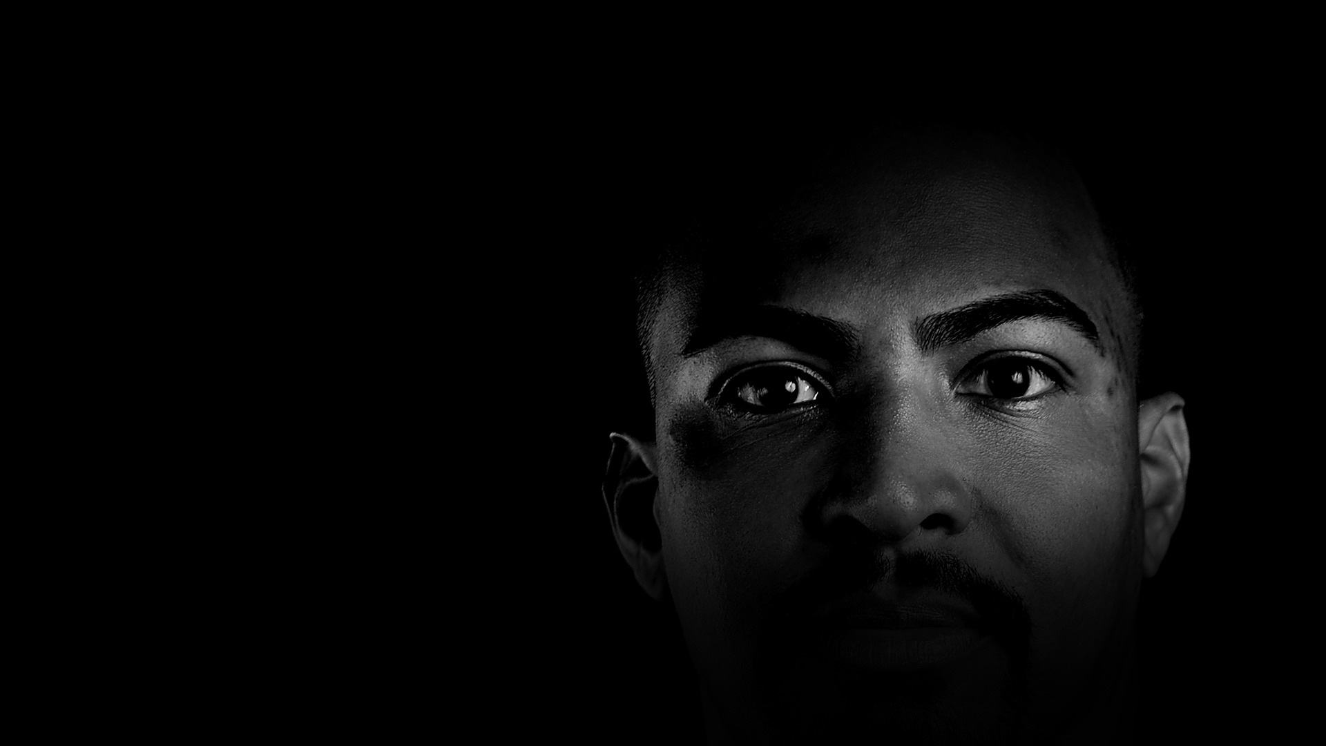 Retrato de Eric Coutinho emergindo do escuro, apenas os olhos iluminados.