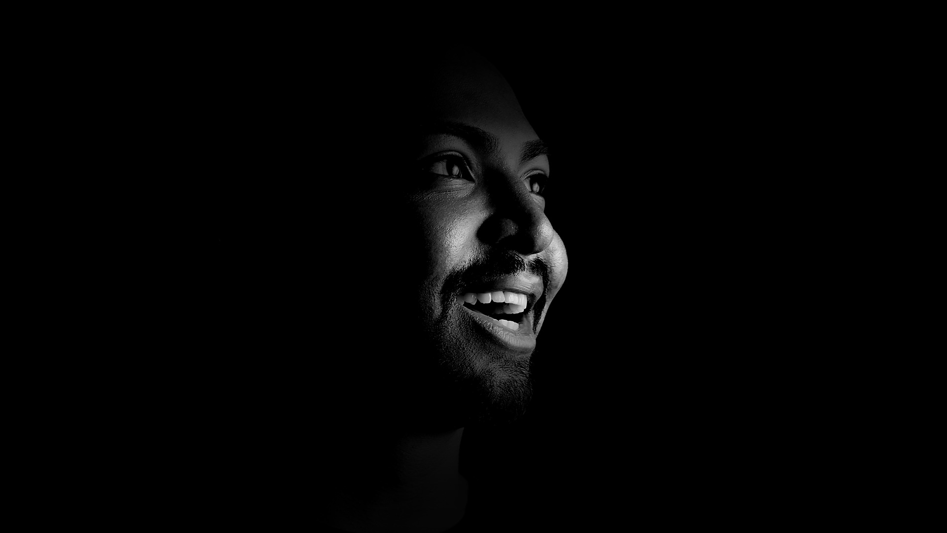 Retrato de Eric Coutinho de camiseta preta, sorrindo, emergindo do escuro.